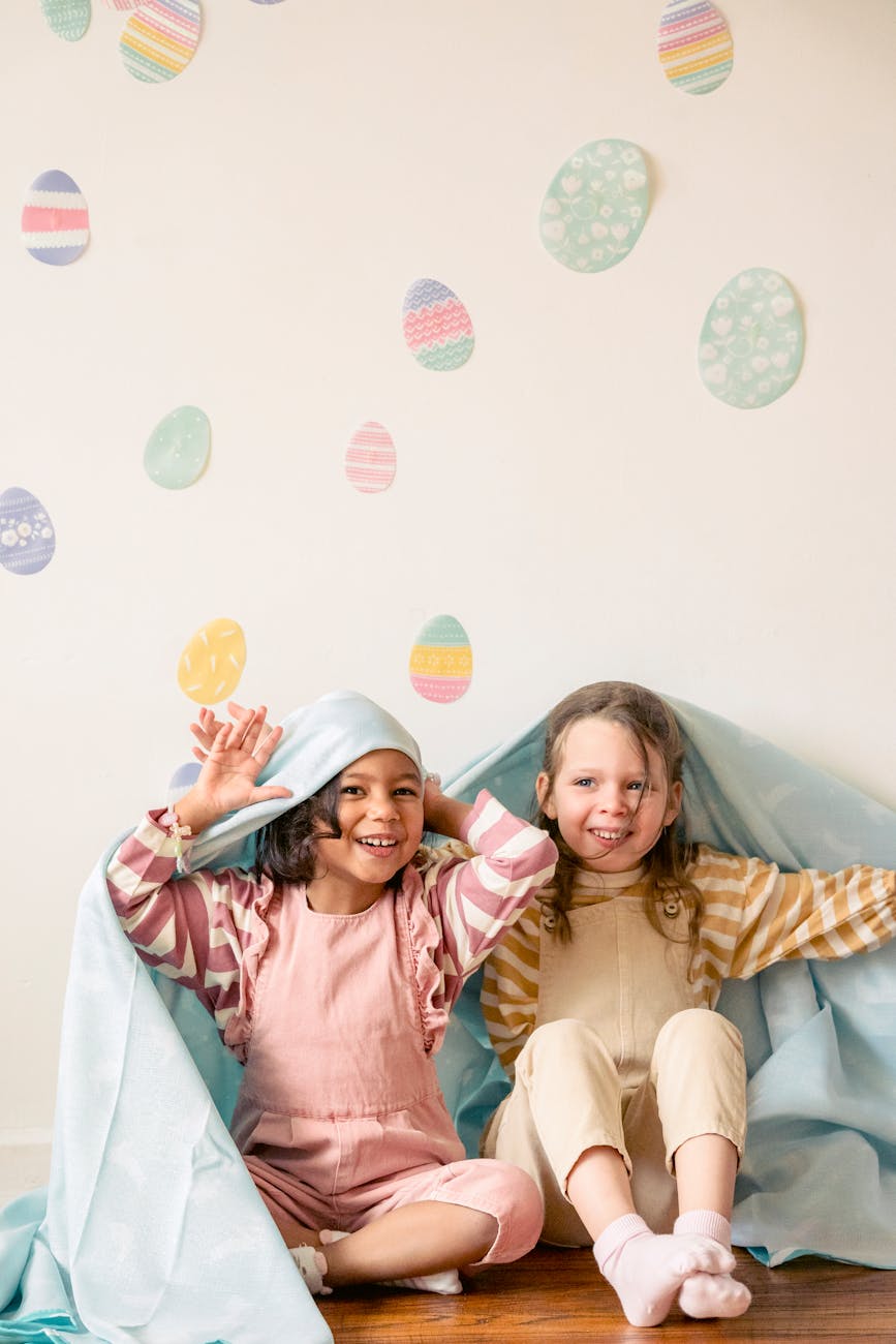 kids sitting on the wooden flooring while hiding under the blanket